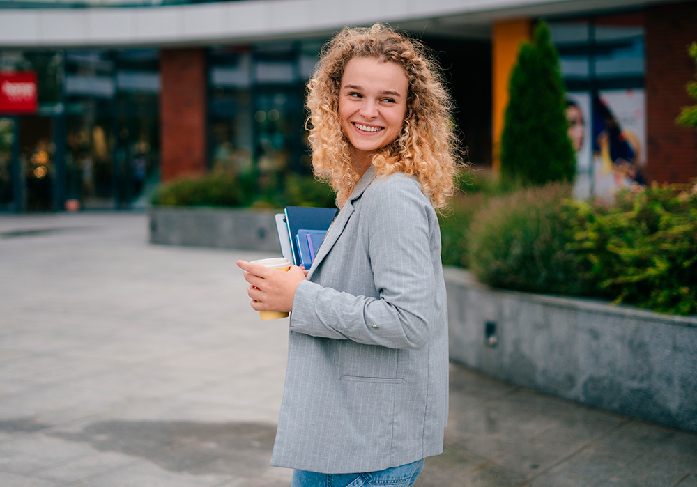Una estudiante sonriente delante de un centro universitario.